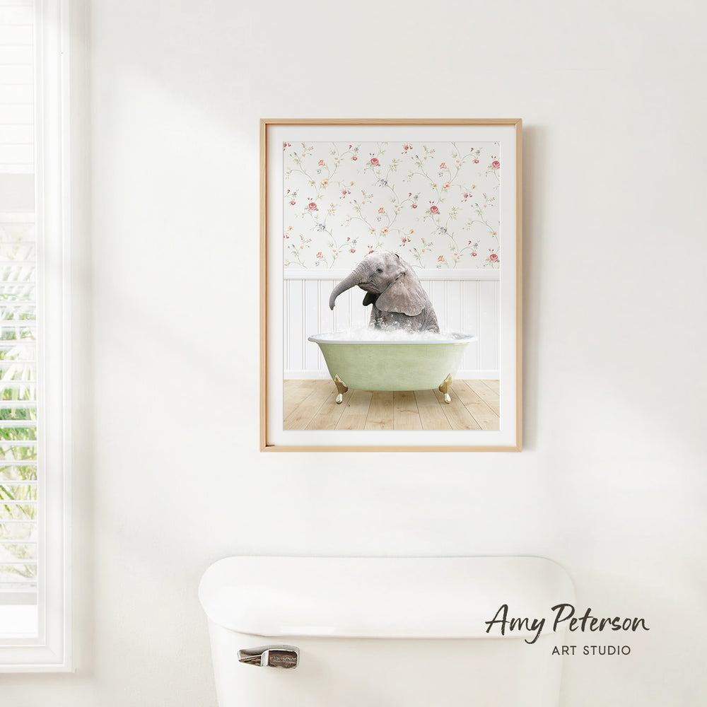 A framed image of a baby elephant sitting in a bathtub, surrounded by a floral pattern on the wall behind it.