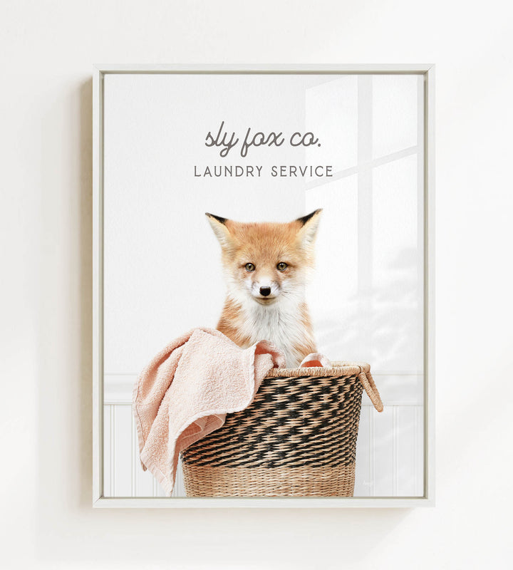 A young fox sits in a woven laundry basket, with a towel draped over its back.