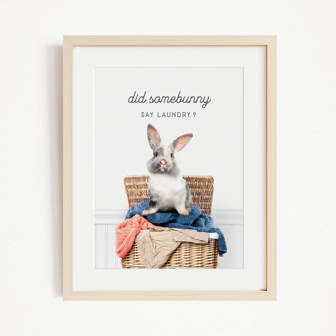 A framed image of a rabbit sitting in a wicker basket filled with laundry, with the text "did some bunny" and "Say laundry?" displayed above the rabbit.