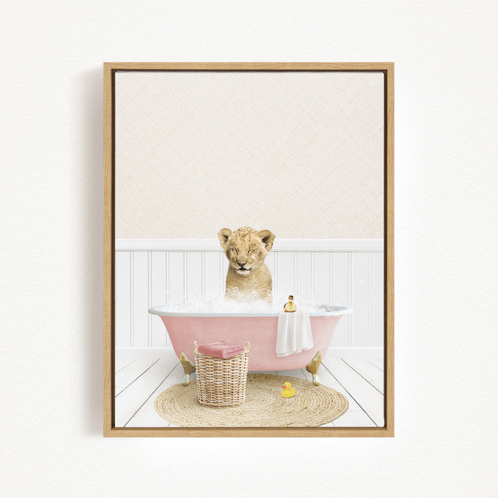 A young lion cub sitting in a pink bathtub filled with bubbles, surrounded by a basket of toys and a yellow rubber ducky.