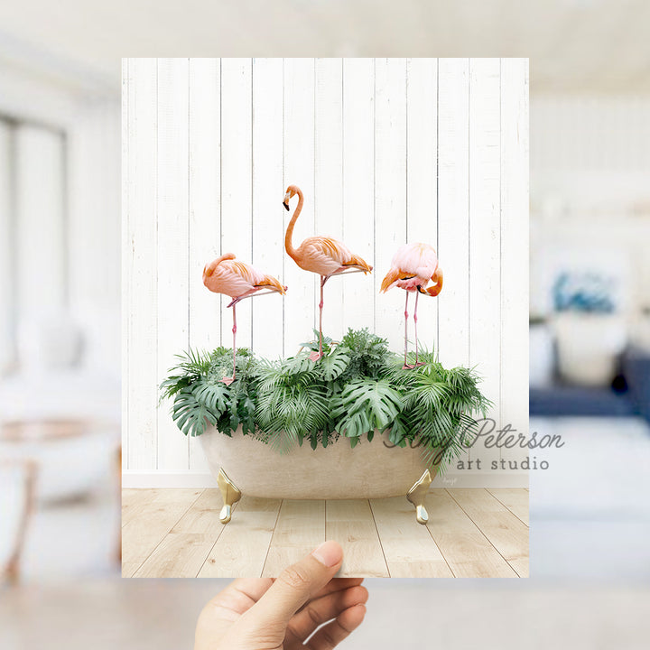 a hand holding a card with three flamingos in a bathtub