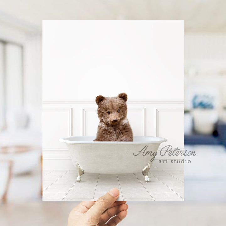 a hand holding a polaroid of a brown bear in a bathtub