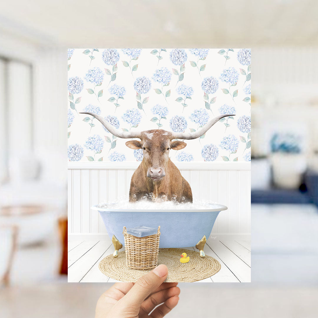 A brown cow with long horns is sitting in a blue bathtub filled with water, surrounded by a floral patterned wall.
