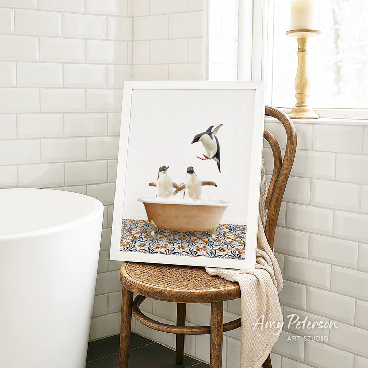 A framed image of two penguins sitting in a bathtub, surrounded by a patterned tile design, is displayed on a wooden chair in a bathroom setting.
