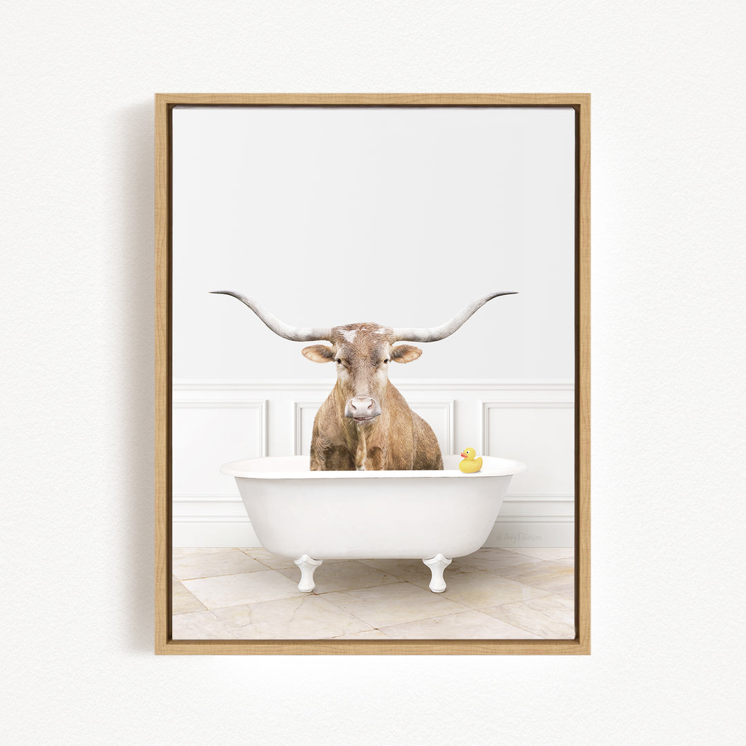 A brown cow with large horns is sitting in a white bathtub, with a yellow rubber duck floating in the water.