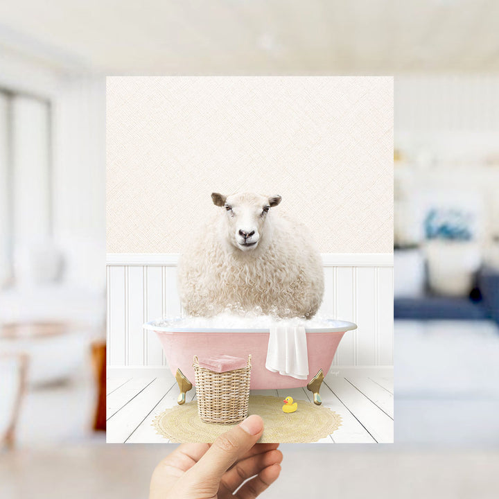 A fluffy white sheep sits in a pink bathtub filled with bubbles, surrounded by a yellow rubber duck and a white towel.