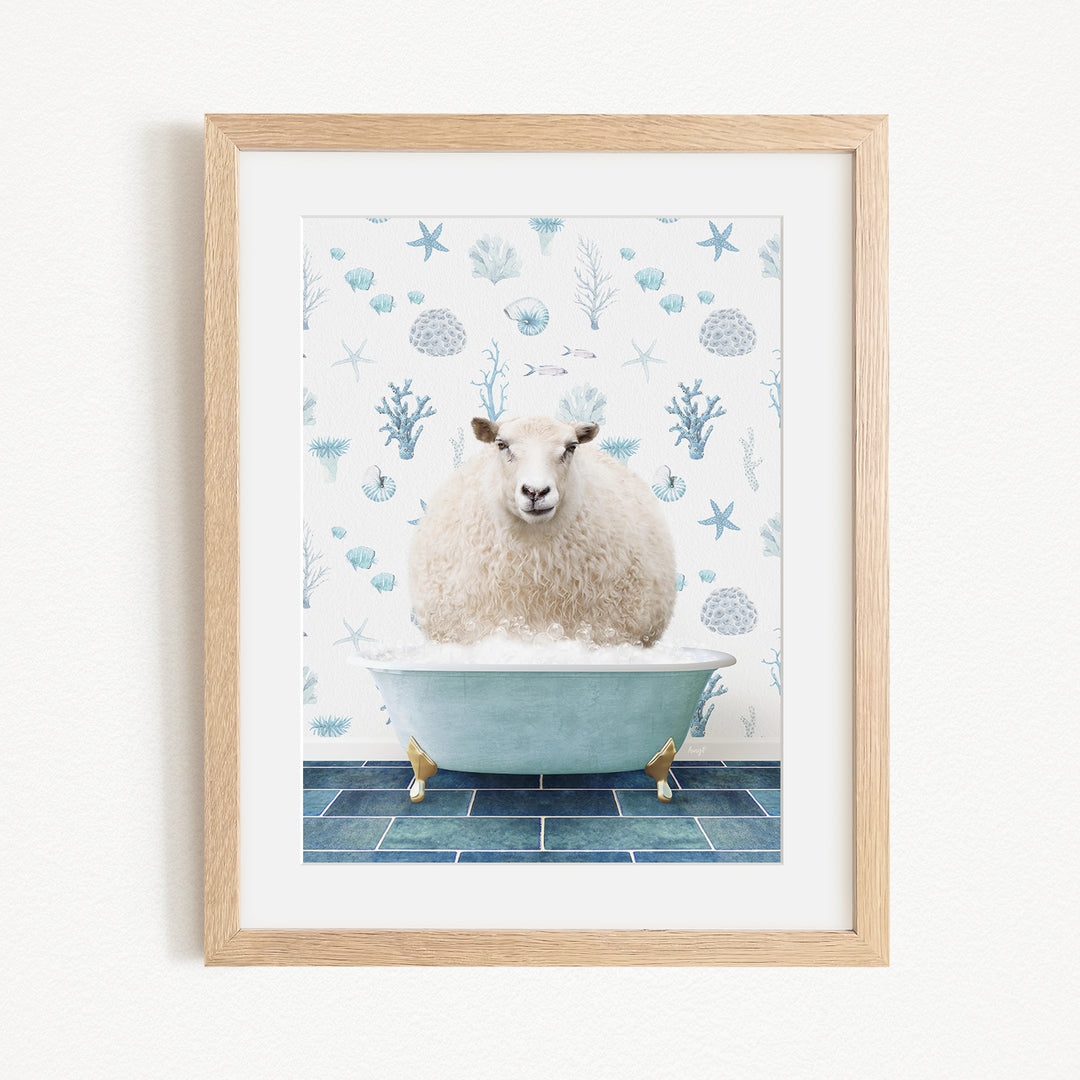 A framed image depicting a fluffy white sheep sitting in a blue bathtub filled with bubbles, surrounded by a pattern of blue and white seashells and starfish.