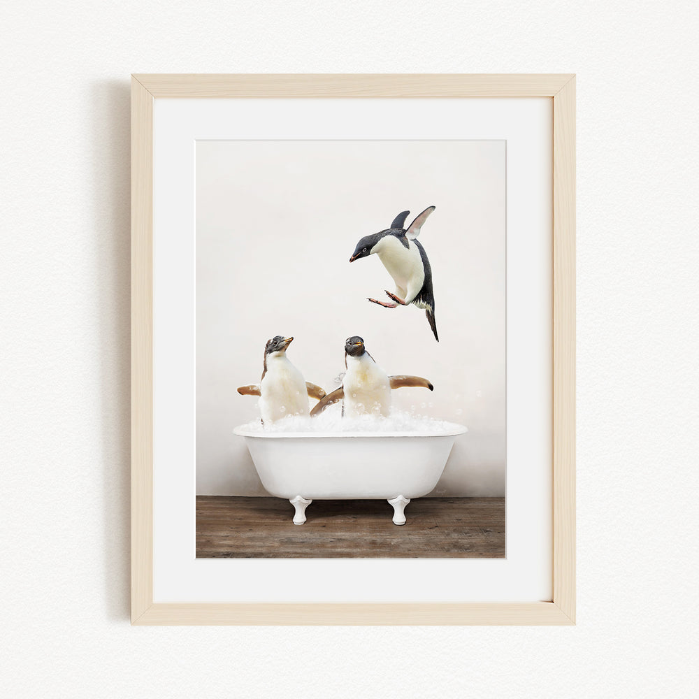 A framed image depicting three penguins sitting in a white bathtub, with one penguin flying towards the others.