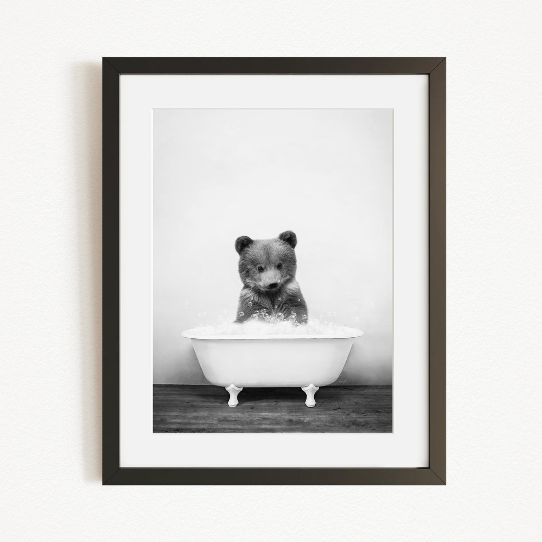 A black and white photograph of a bear sitting in a bathtub filled with water.