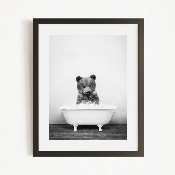 A black and white photograph of a bear sitting in a bathtub filled with water.