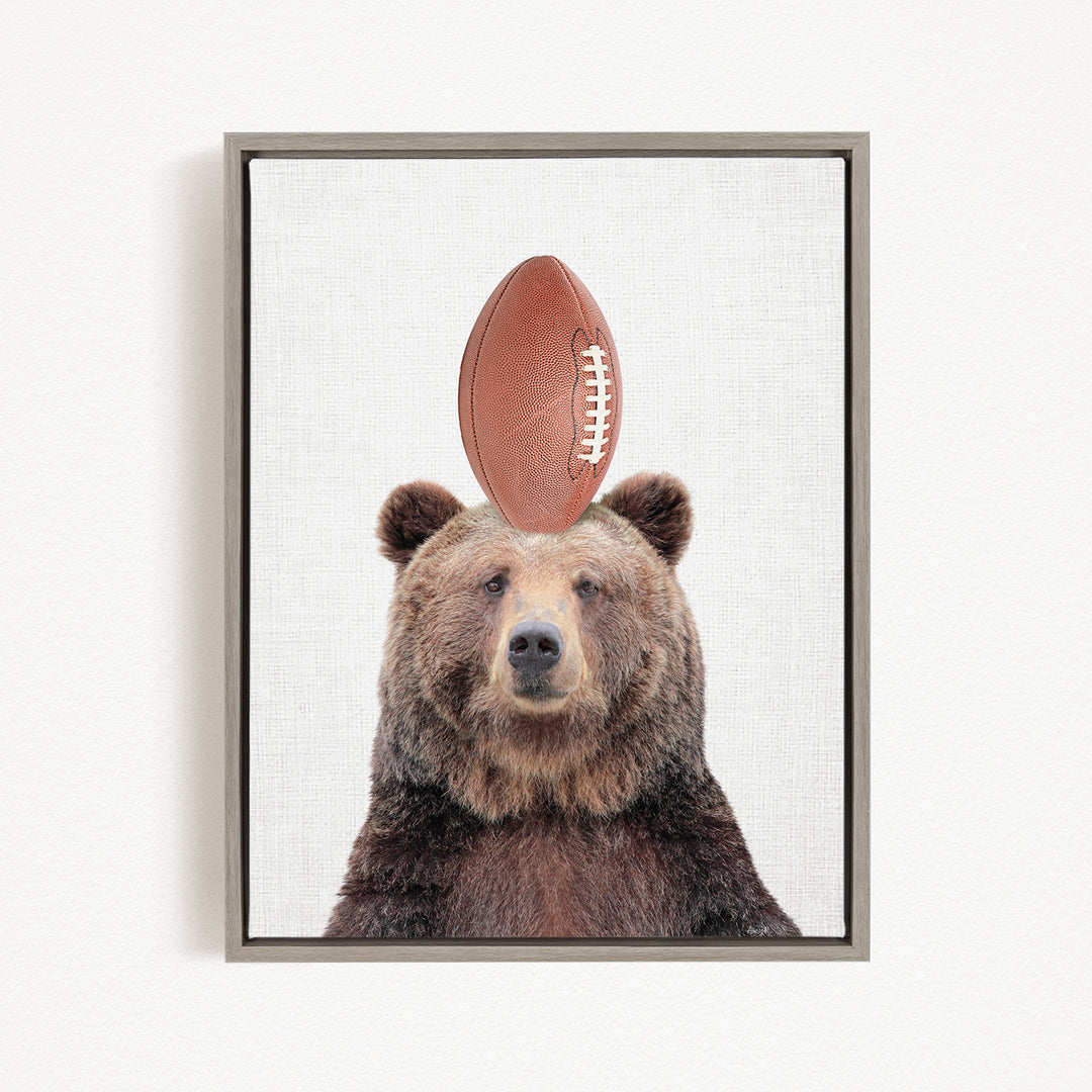 A brown bear standing on a football with its head tilted upwards.