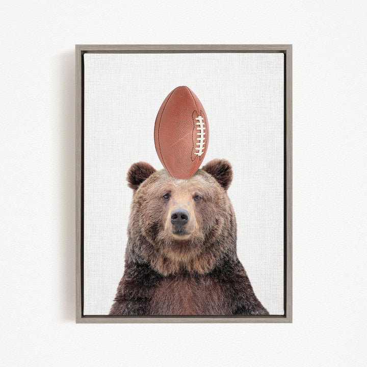 A brown bear standing on a football with its head tilted upwards.