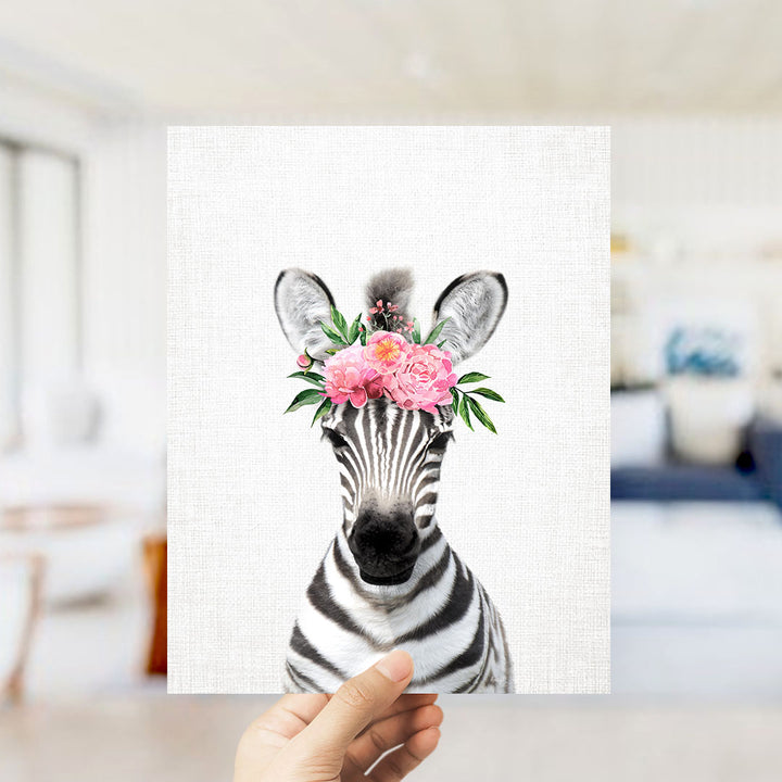 A hand is holding up a framed print of a zebra wearing a floral headpiece.