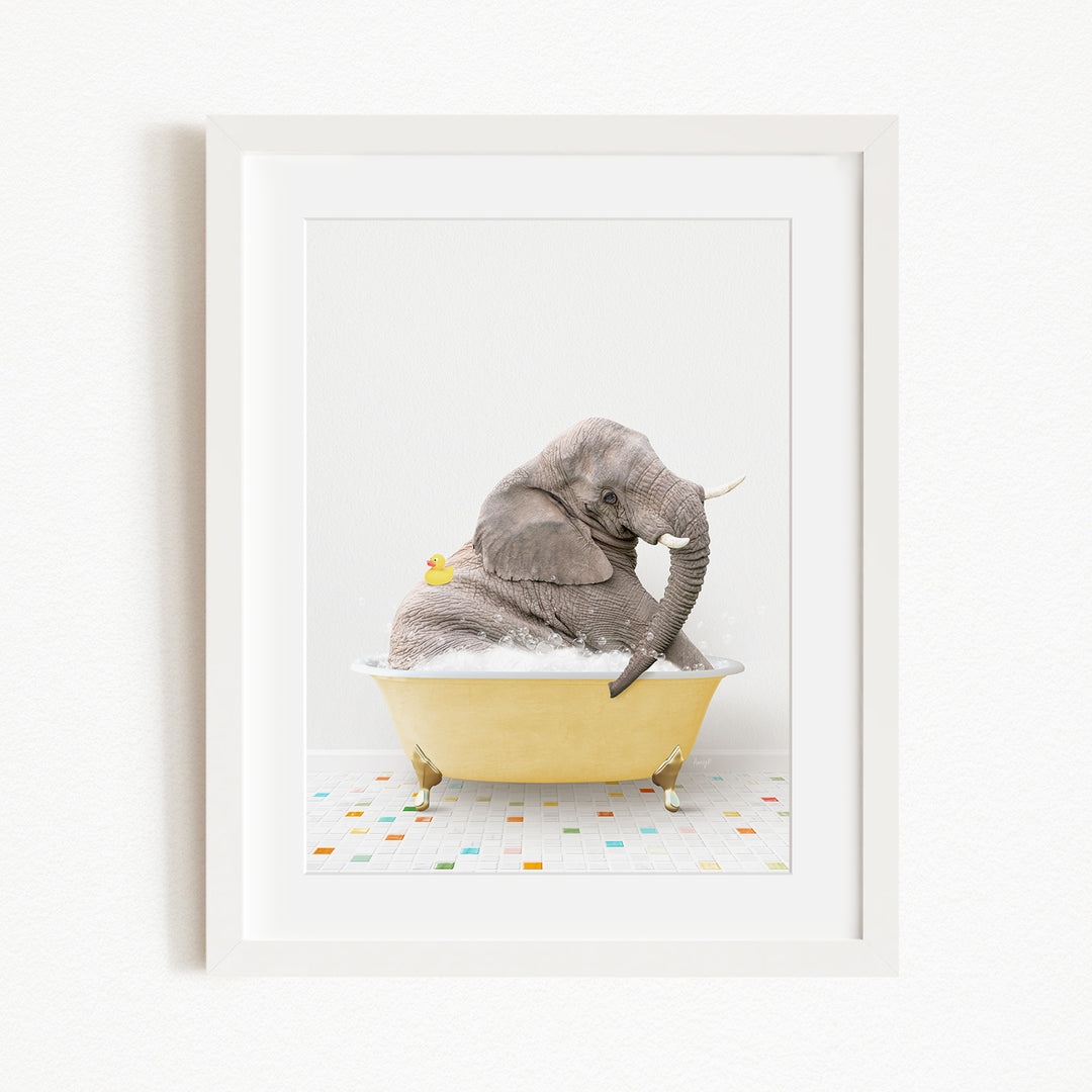 A gray elephant is sitting in a yellow bathtub filled with bubbles, with a yellow rubber duck floating on the water.