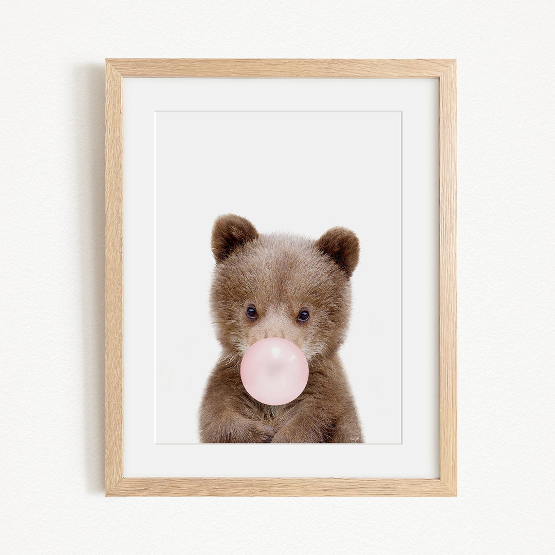 A cute brown bear is blowing a bubble with a pink bubble gum bubble.