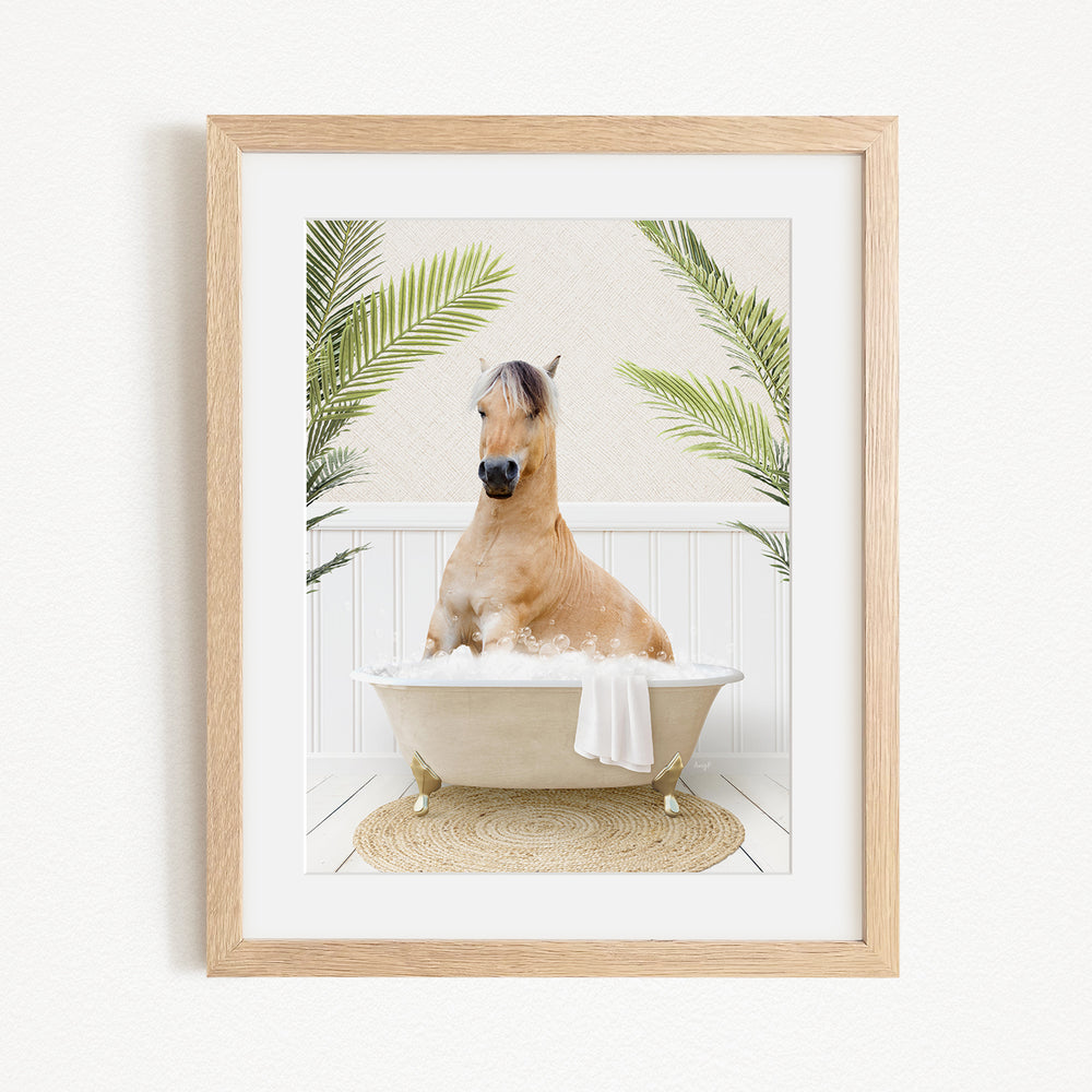 A light brown horse is sitting in a white bathtub filled with water, surrounded by green palm leaves.