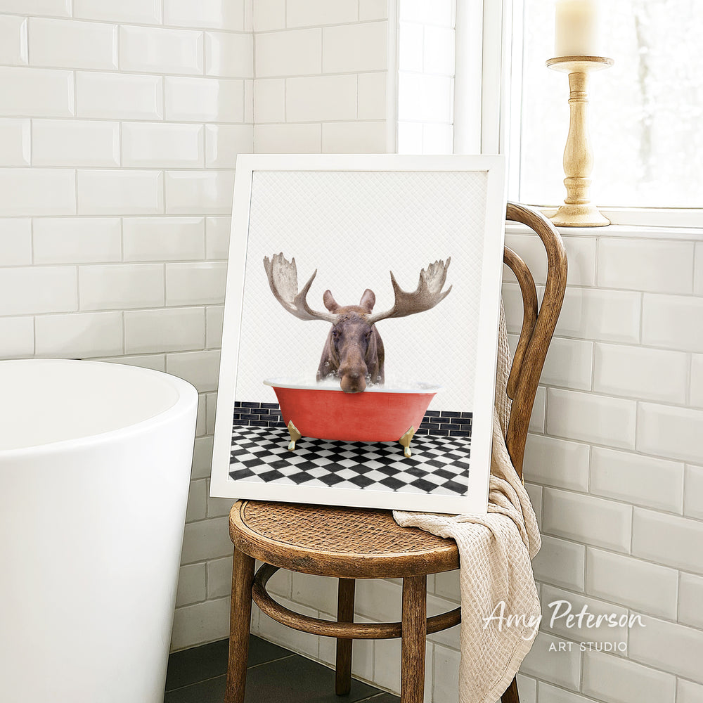 A framed image of a moose with antlers sitting in a red bathtub, surrounded by a black and white checkered floor.