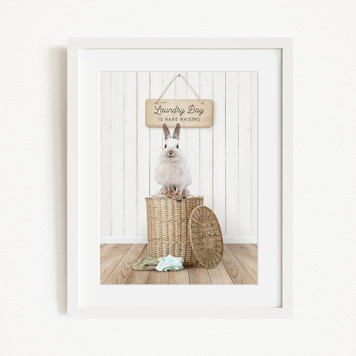 A white rabbit sits atop a wicker laundry basket, with a wooden sign above that reads "Laundry Day is hard washing".