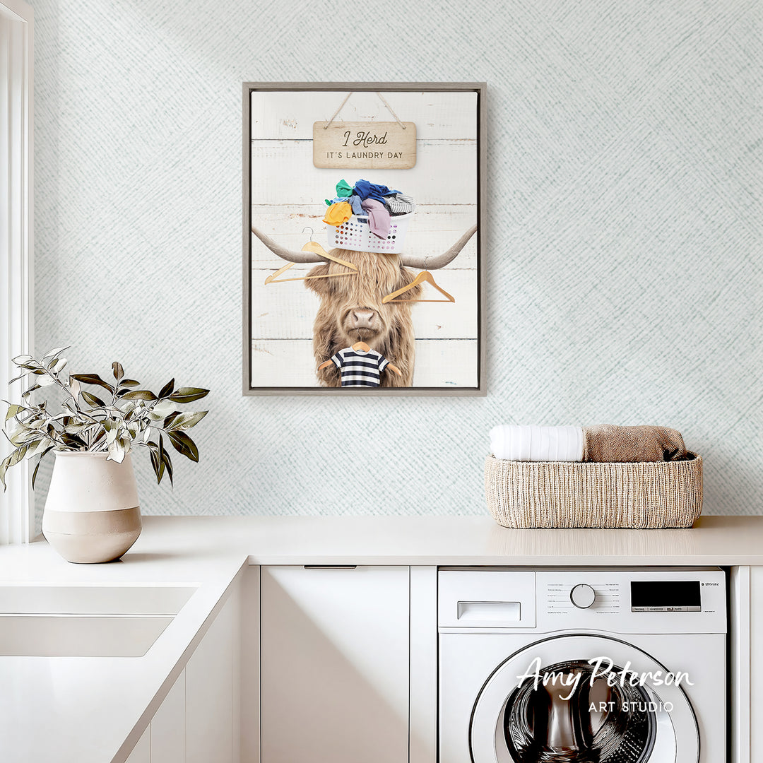 a framed print of a cow with a basket on its head, hanging on a wall above a white countertop with a plant and a basket of towels.