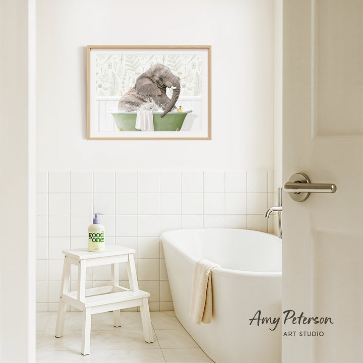 A framed painting of an elephant in a bathtub hangs on a white tiled wall above a white bathtub in a bathroom.