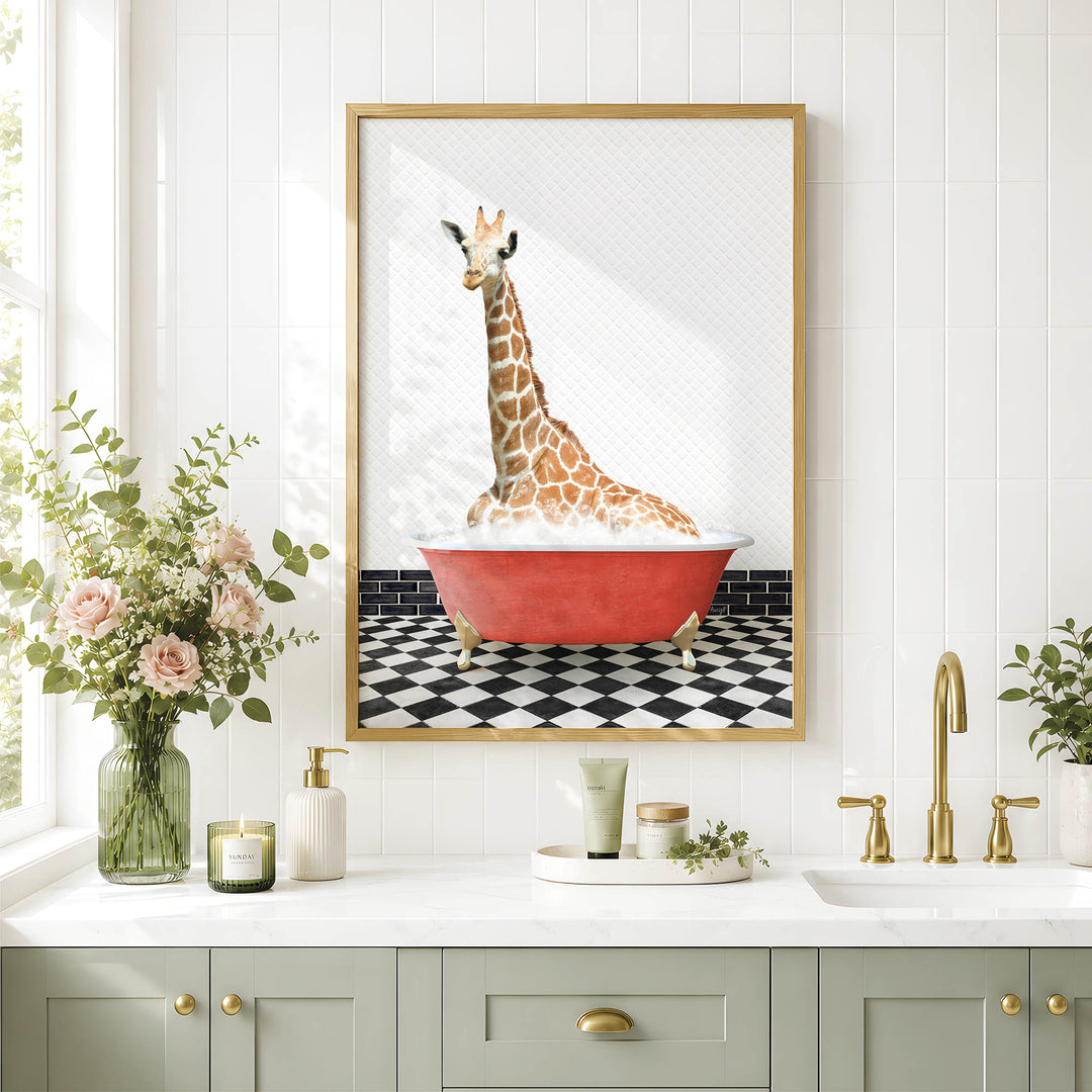 A framed image of a giraffe sitting in a red bathtub is displayed on a white wall above a bathroom counter with various toiletries and a vase of flowers.