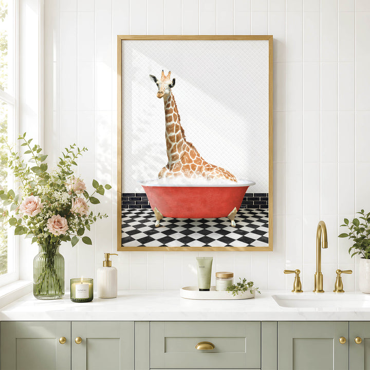 A framed image of a giraffe sitting in a red bathtub is displayed on a white wall above a bathroom counter with various toiletries and a vase of flowers.