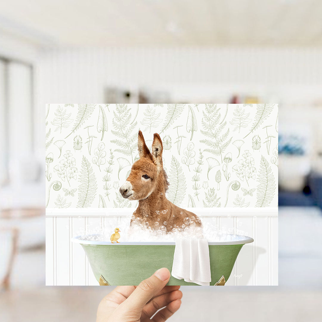 A hand holding a framed image of a kangaroo sitting in a bathtub, surrounded by a green tub and a small yellow duck.