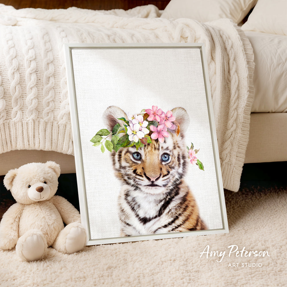 A framed print of a tiger cub wearing a flower crown is displayed on a beige carpet, accompanied by a teddy bear.