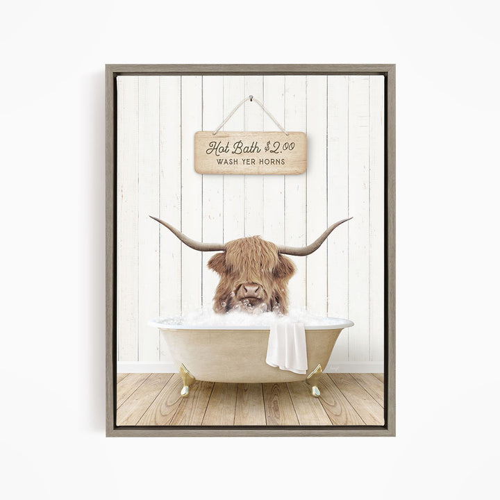A framed image depicting a Highland cow with long horns sitting in a bathtub, with a sign above the bathtub that reads "Hot Bath $2.00 WASH YER HORSES".