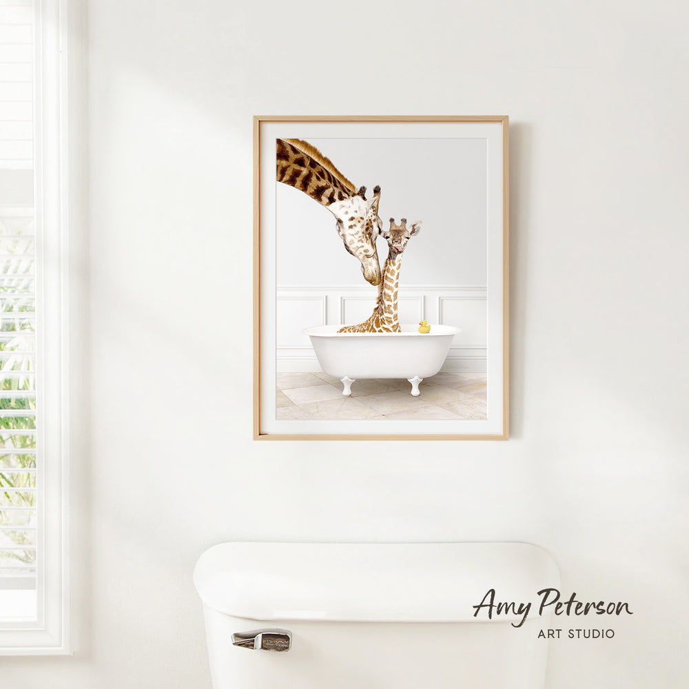 A framed image of two giraffes sitting in a white bathtub, with one giraffe reaching up to the other.