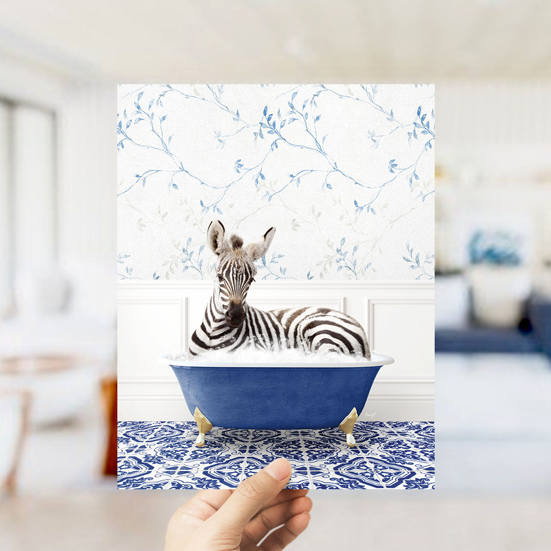 A zebra is sitting in a blue bathtub, surrounded by a patterned blue and white rug, in a room with a floral wallpaper.