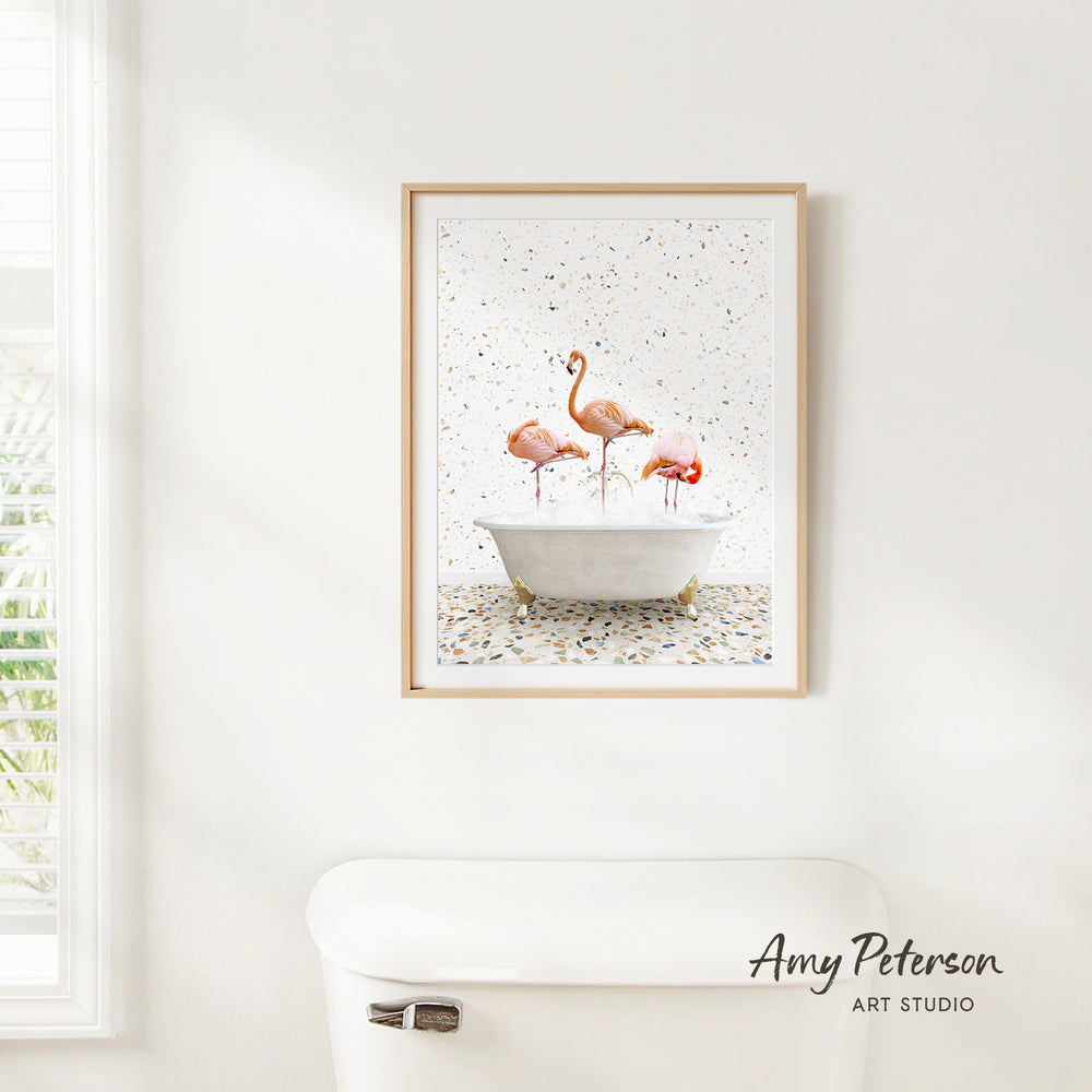 A framed painting of three flamingos standing in a white bathtub, with a window and toilet visible in the background.