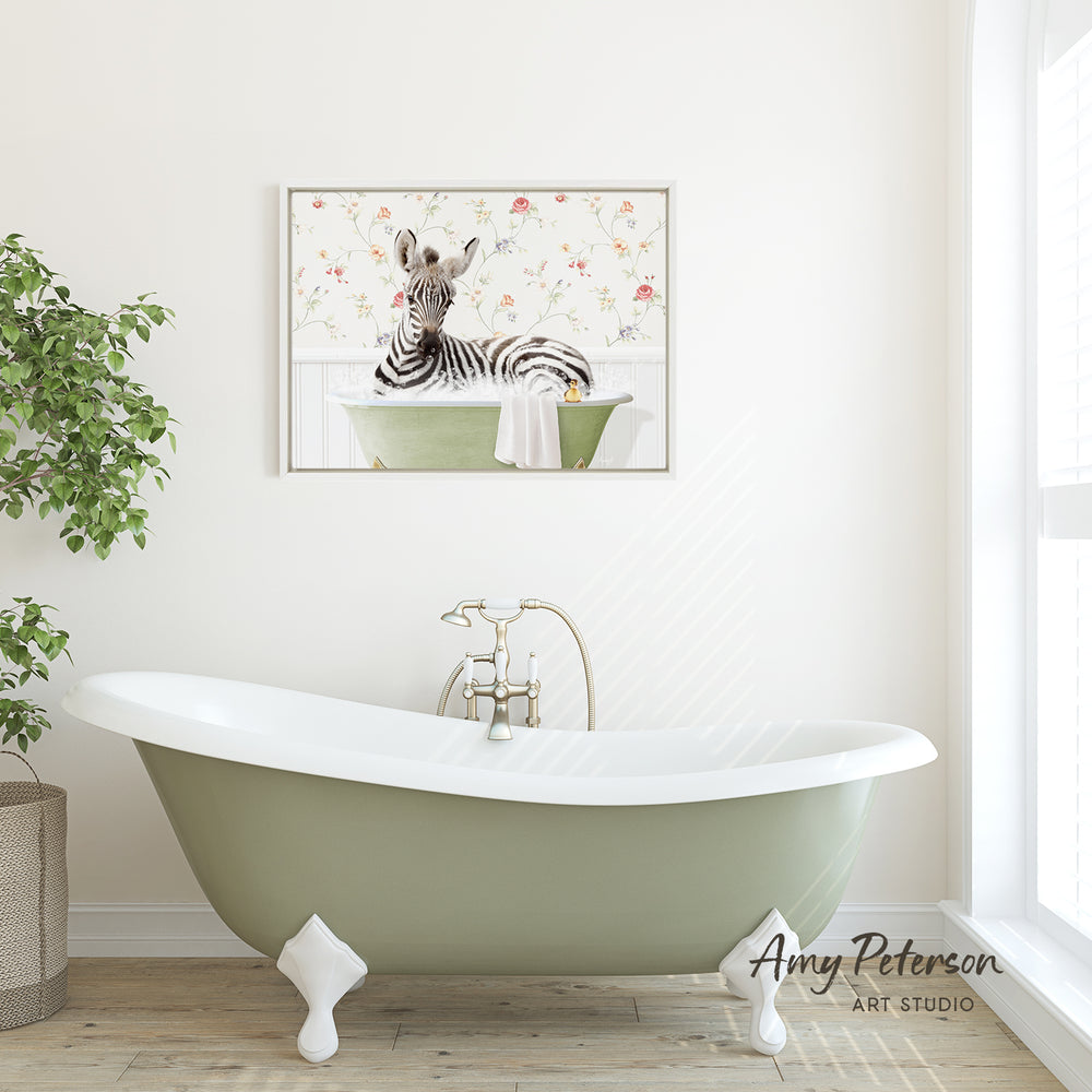 A green clawfoot bathtub with a zebra sitting in it, set against a white wall with a framed picture of a zebra above it.