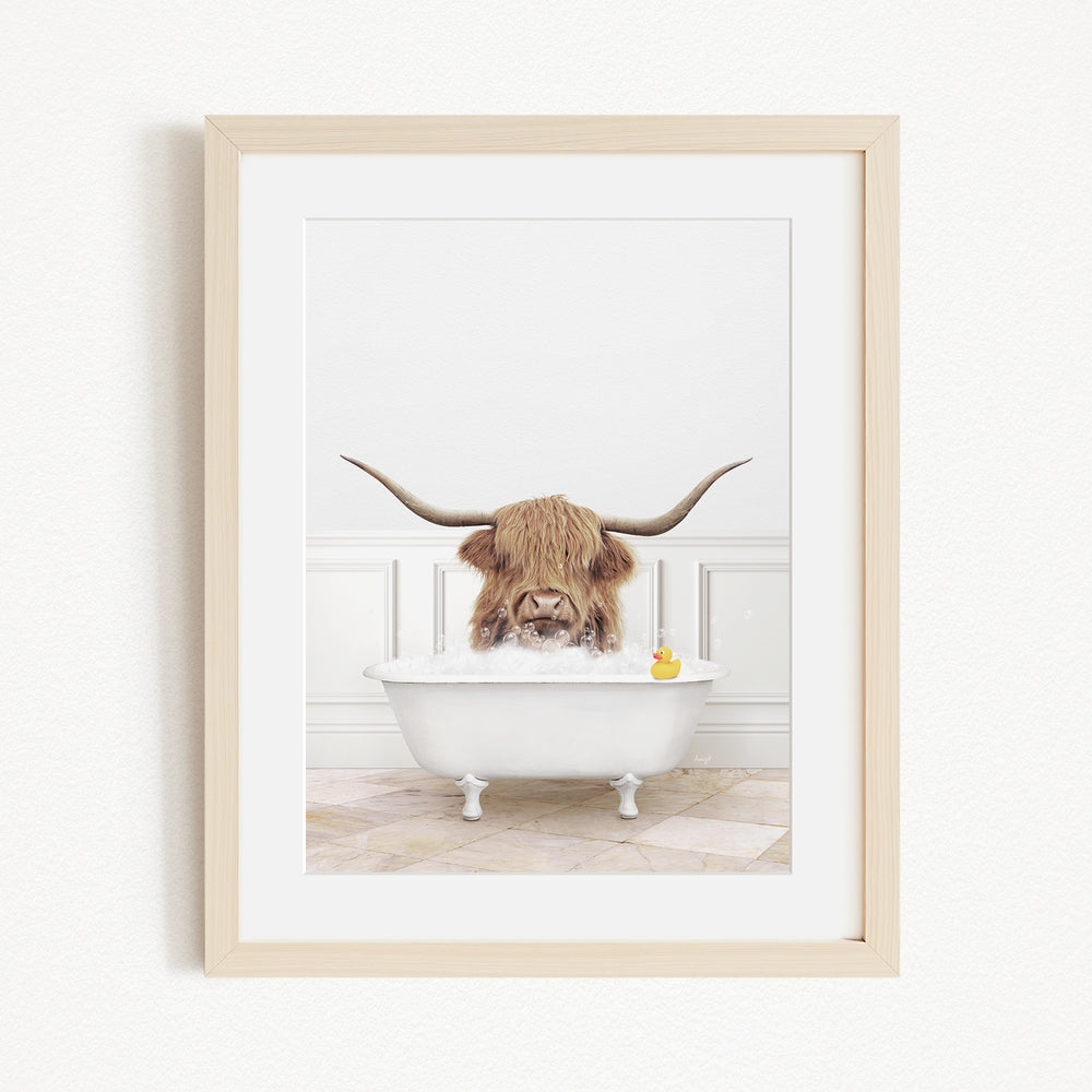A Highland cow with large horns is sitting in a white bathtub, surrounded by a yellow rubber duck.