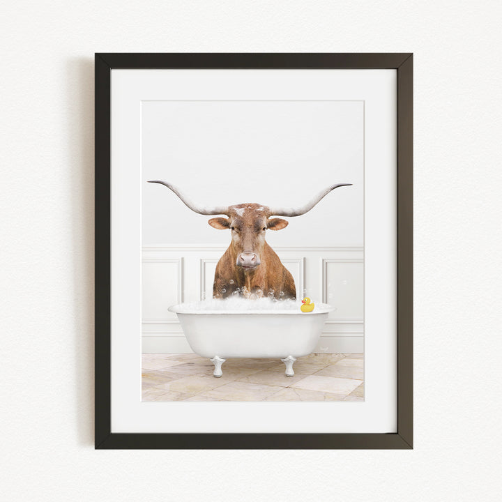 A brown cow with long horns is sitting in a white bathtub filled with water, with a yellow rubber duck floating in the tub.