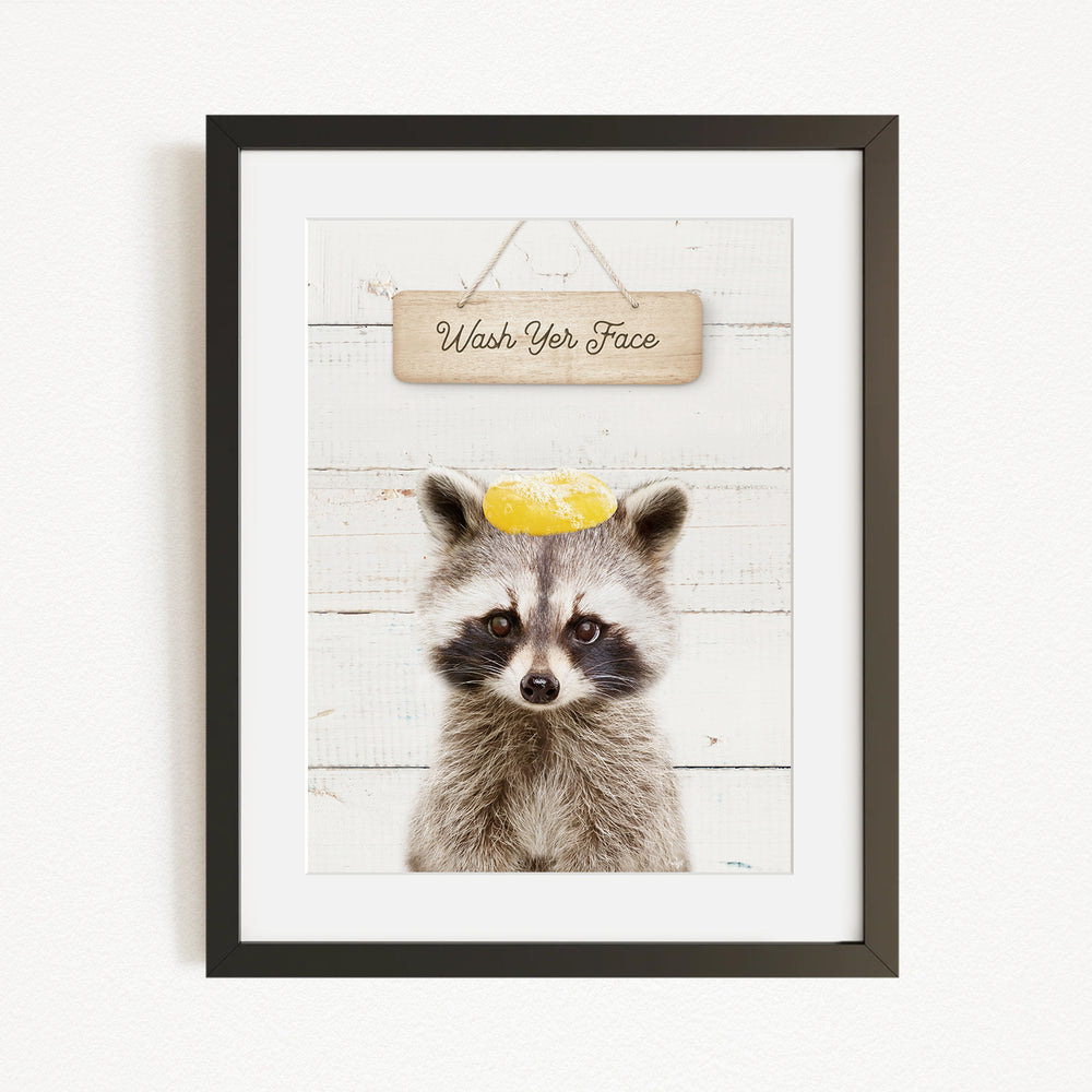 A raccoon wearing a yellow hat with the text "Wash Your Face" written on it, set against a white wooden background.