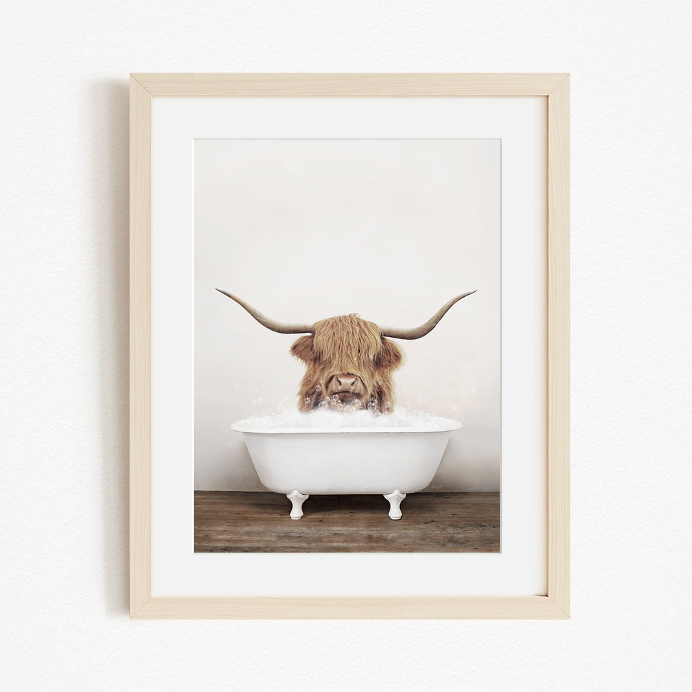 A Highland cow with long horns is sitting in a white bathtub filled with water, creating a whimsical and playful scene.
