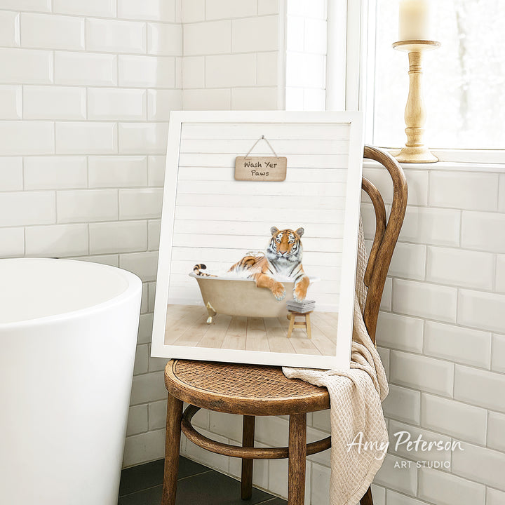 A framed print of a tiger sitting in a bathtub, with a sign that says "Wash Your Pants" hanging above it. The print is displayed on a wooden chair in a bathroom setting.