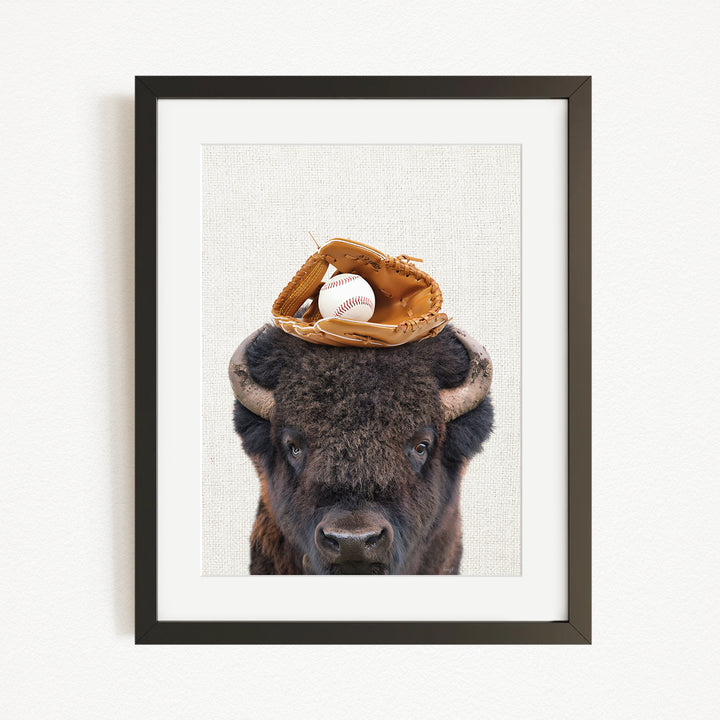 A buffalo with a baseball glove on its head is the main subject of the framed image.