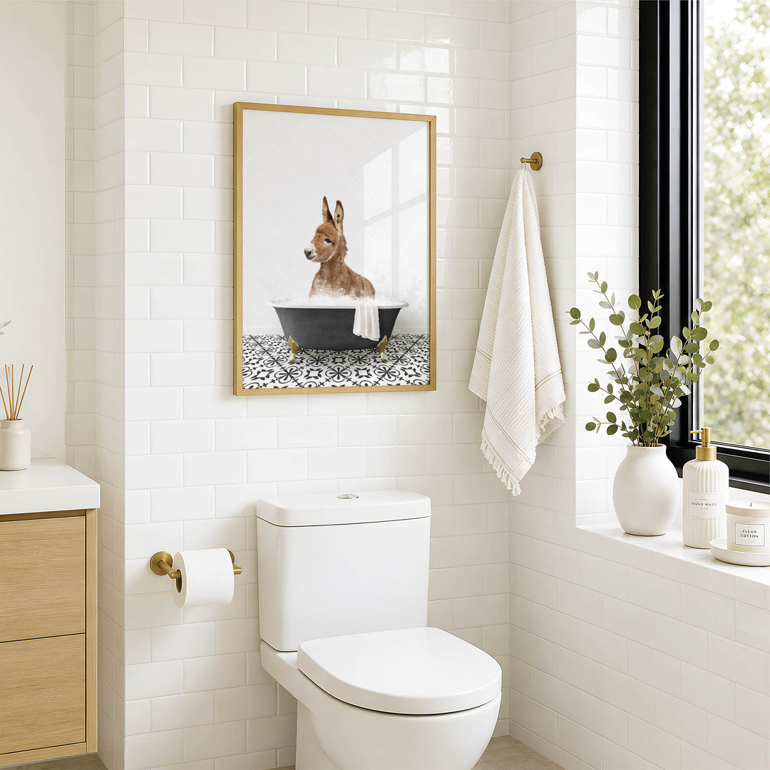 A bathroom with a white toilet, a framed picture of a donkey in a bathtub, and a towel rack with a towel.