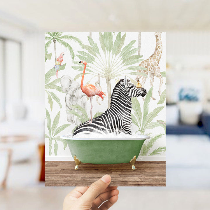 A hand holds up a framed print featuring a vibrant illustration of a zebra sitting in a green bathtub, surrounded by various tropical animals such as a flamingo, a giraffe, and a monkey.