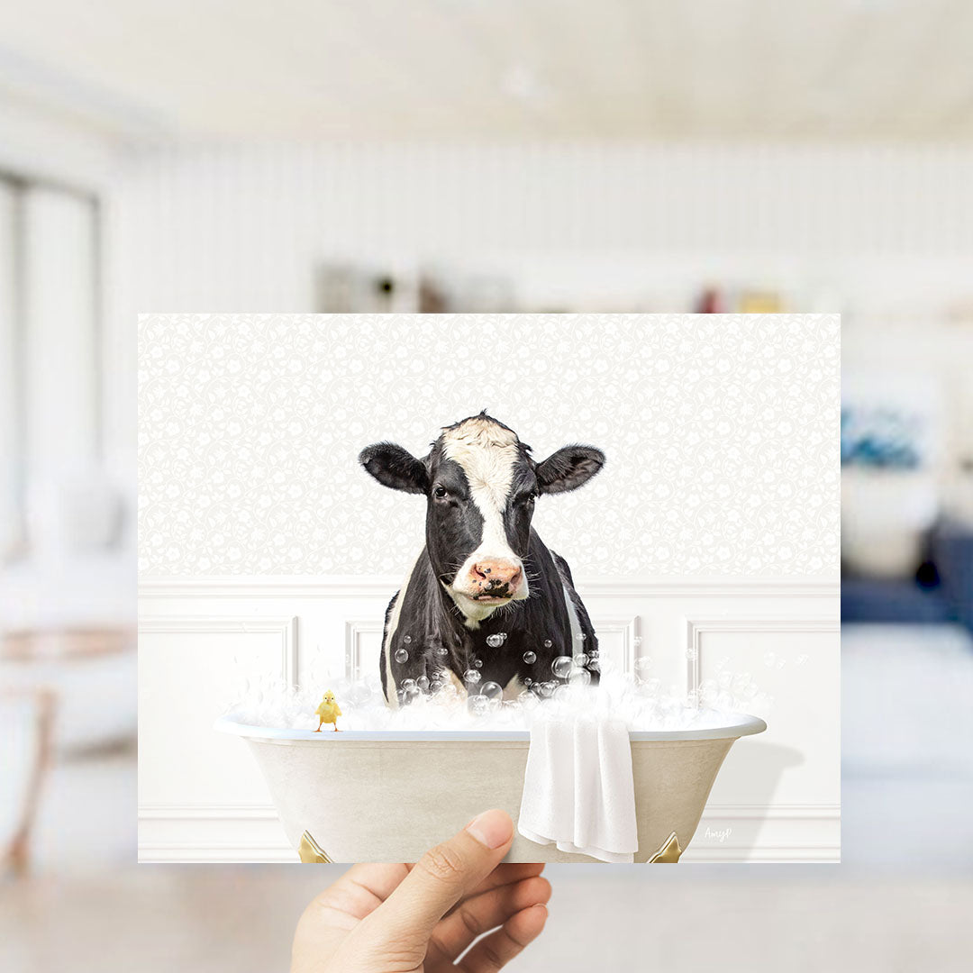A black and white cow is sitting in a bathtub filled with bubbles, with a small yellow bird perched on the edge of the tub.