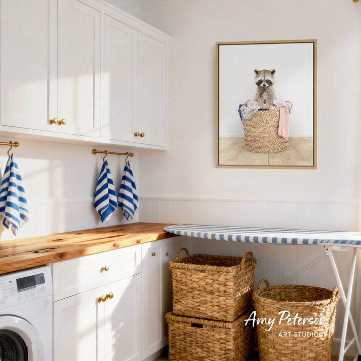 A laundry room with white cabinets, a wooden countertop, and a framed picture of a raccoon sitting in a basket.