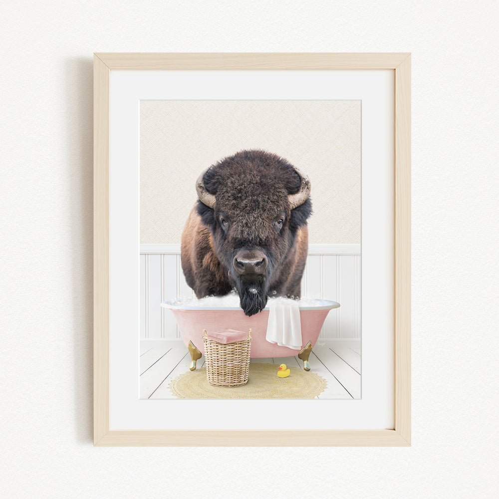 A buffalo standing in a pink bathtub, with a basket of rubber ducks nearby.