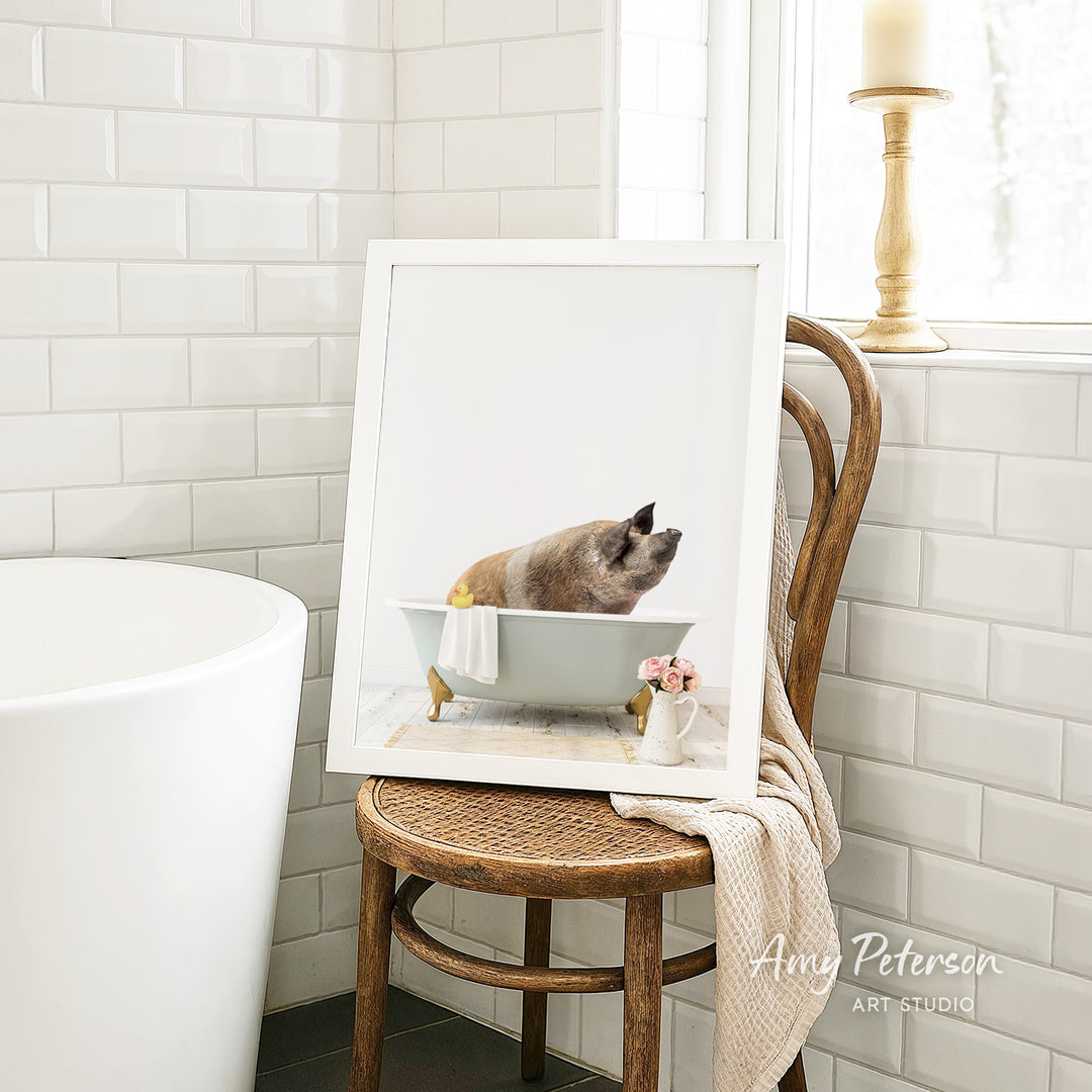 A framed image of a cat sitting in a bathtub, with a vase of flowers and a candle on a chair in the background.