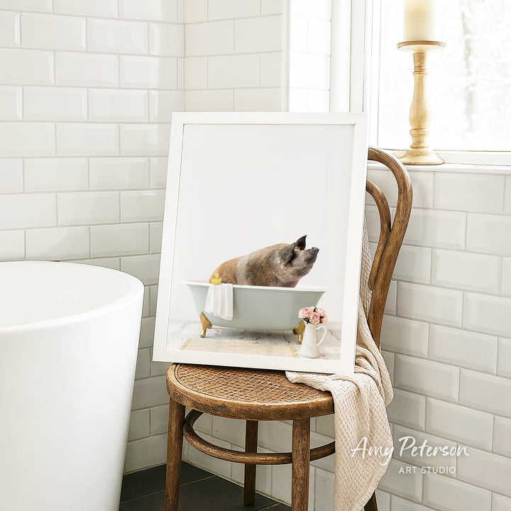 A framed image of a cat sitting in a bathtub, with a vase of flowers and a candle on a chair in the background.