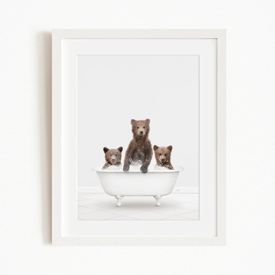 A framed image depicting three brown bears sitting in a white bathtub.