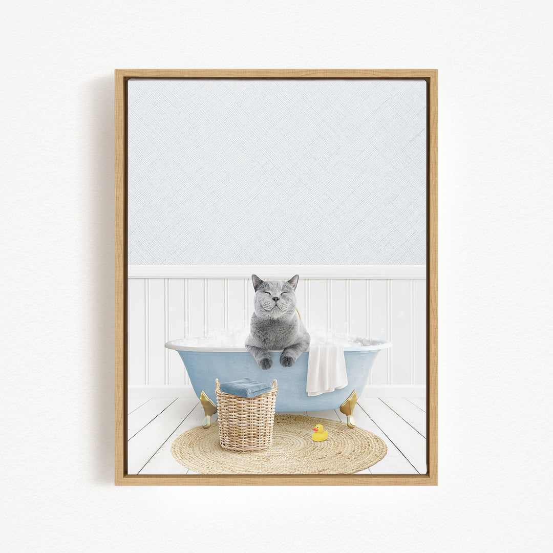 A gray cat sitting in a blue bathtub filled with bubbles, surrounded by a yellow rubber duck and a woven basket.