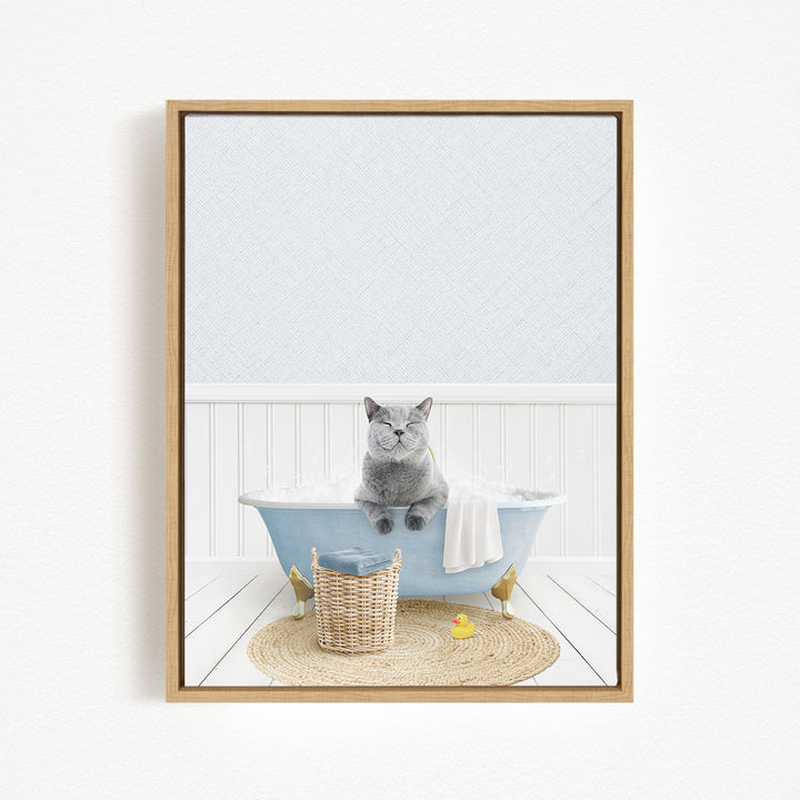 A gray cat sitting in a blue bathtub filled with bubbles, surrounded by a yellow rubber duck and a woven basket.