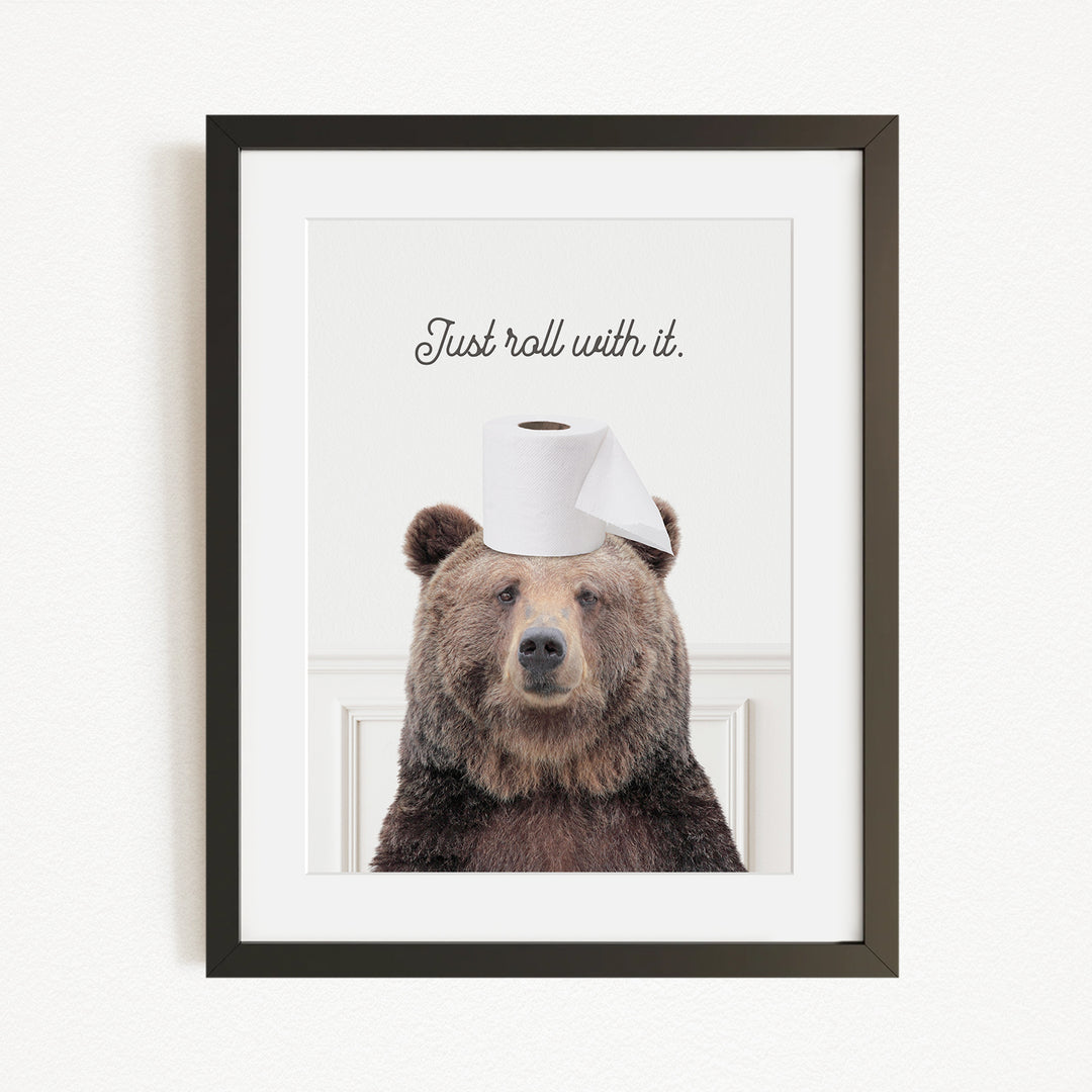 A framed image of a brown bear wearing a toilet paper roll on its head, with the text "Just roll with it."